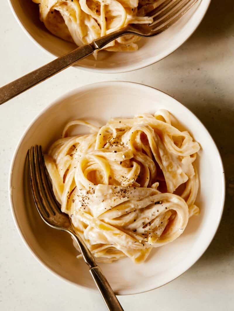 Two bowls of fettuccine alfredo with a fork in one. 