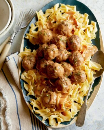 Grass fed lamb meatballs with gravy over egg noodles with forks.