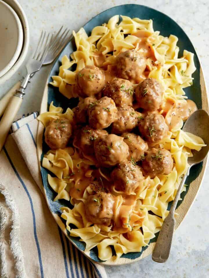 Grass fed lamb meatballs with gravy over egg noodles with forks.