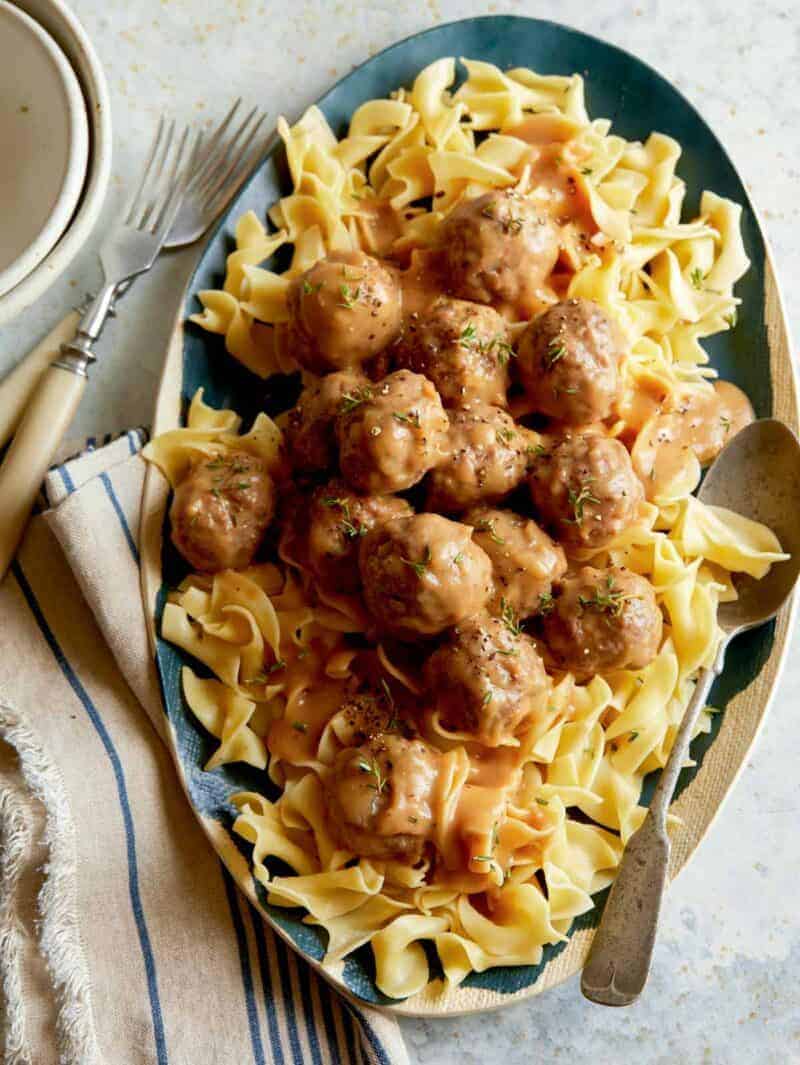 A recipe for Lamb Meatballs with a gravy sauce over a bed of egg noodles on a platter ready to be served. 