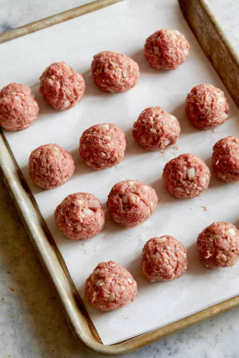 Lamb meatballs rolled and lined up a baking sheet ready to be cooked. 