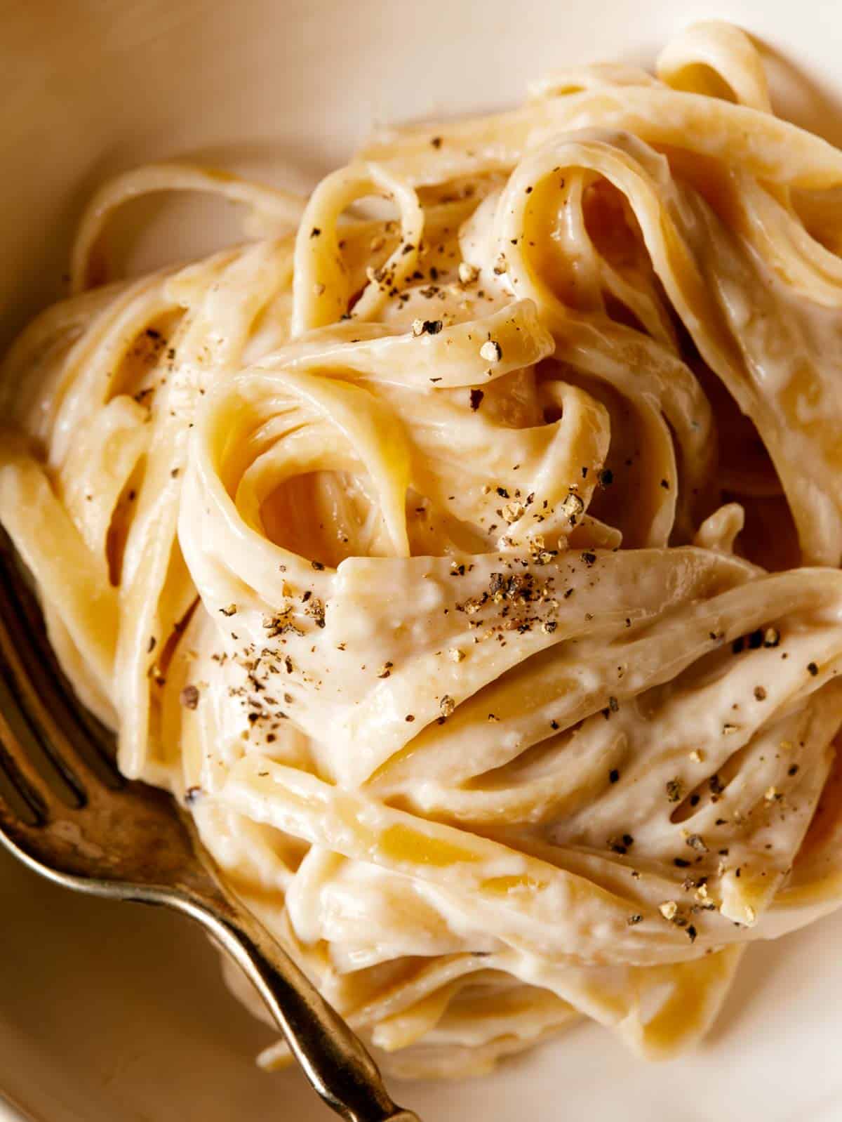 A close up of one pot fettuccine alfredo with cracked black pepper and a fork.