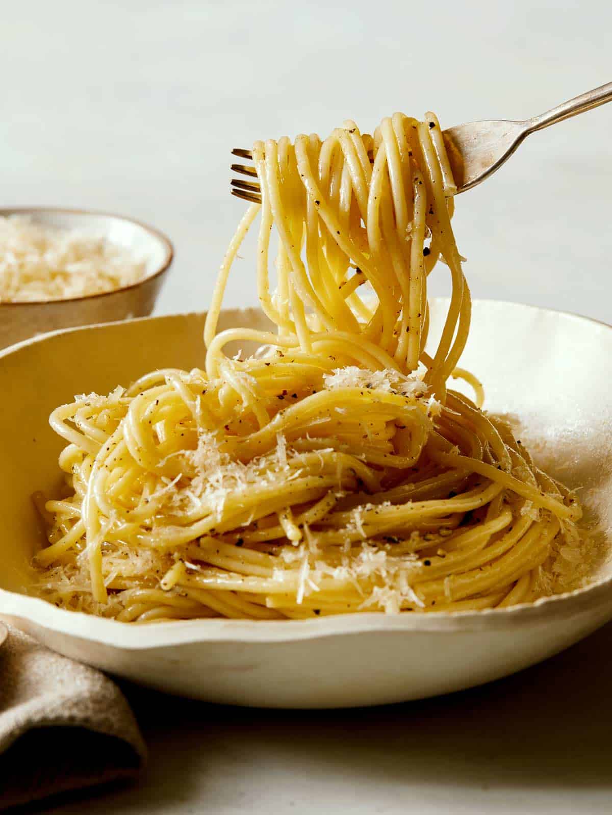 A close up of a bowl of cacio e pepe, twirled on a fork.