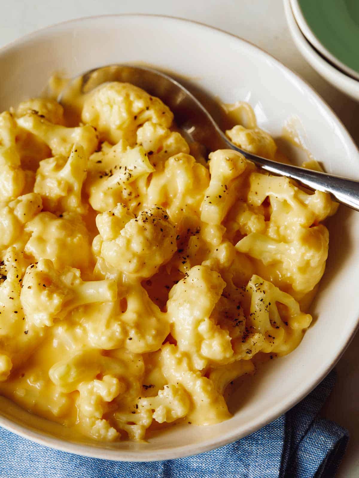 Creamy Cauliflower Mac and Cheese in a bowl with a spoon it and some bowls on the side. 