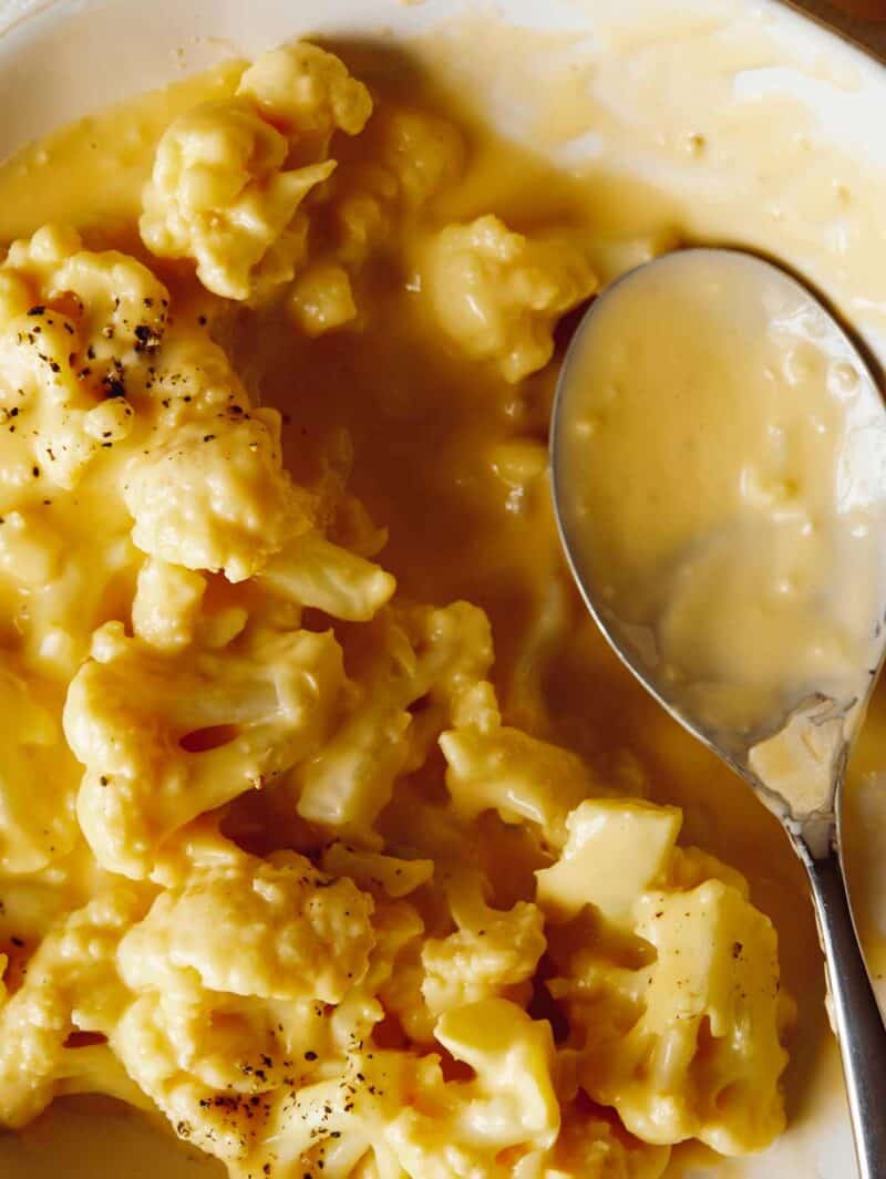 close up of partially filled cheesy cauliflower mac and cheese and serving spoon sitting in bowl