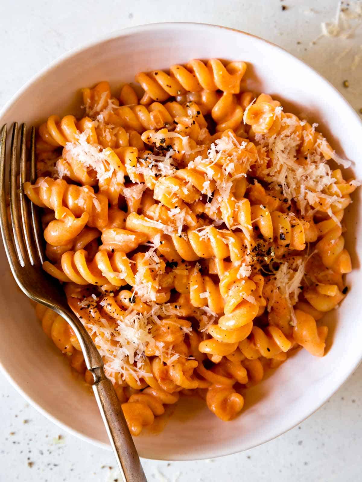 A close up of a bowl of fusilli pasta with vodka sauce and a fork.