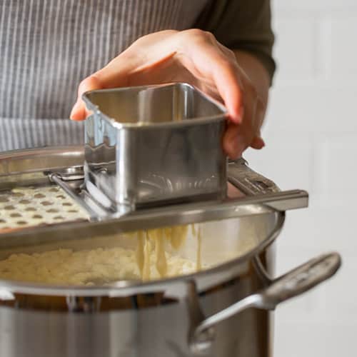 A person making spaetzle over a pot.