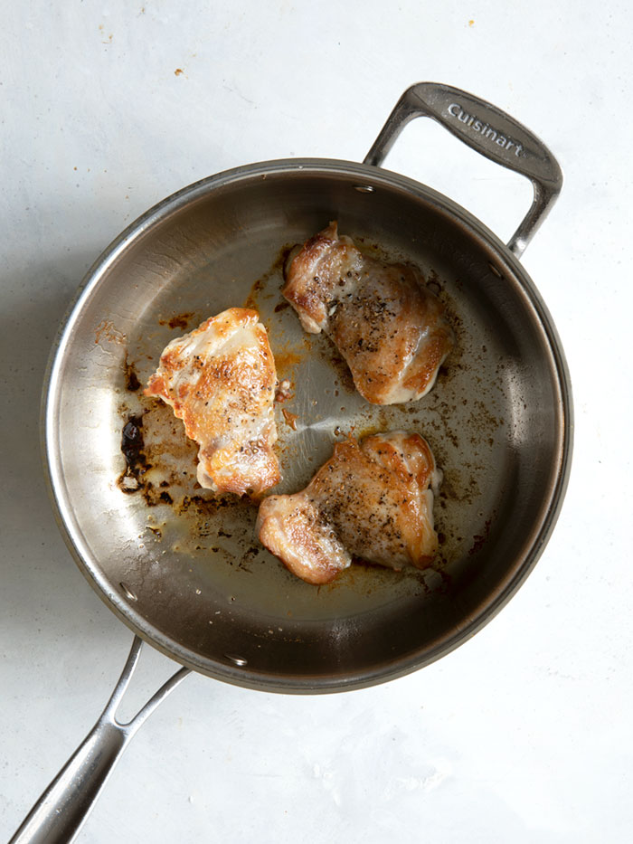 Seared chicken thighs in a skillet with salt and pepper.
