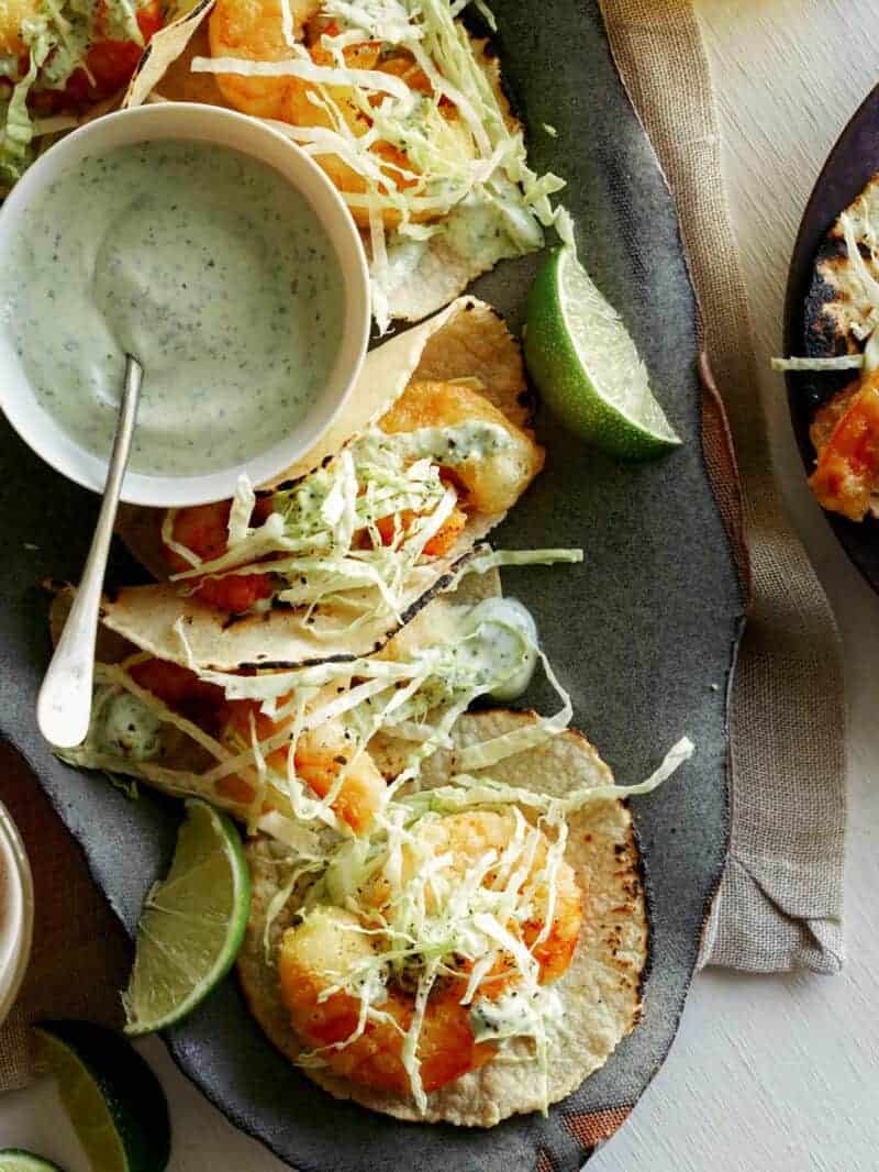 A close up of beer battered fried shrimp tacos with crispy slaw, sauce, and lime.