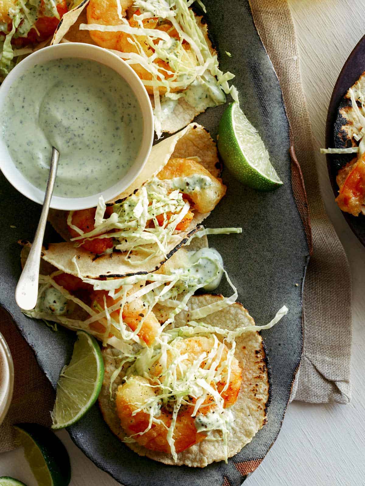 Beer battered shrimp tacos on a plate with lime wedges. 