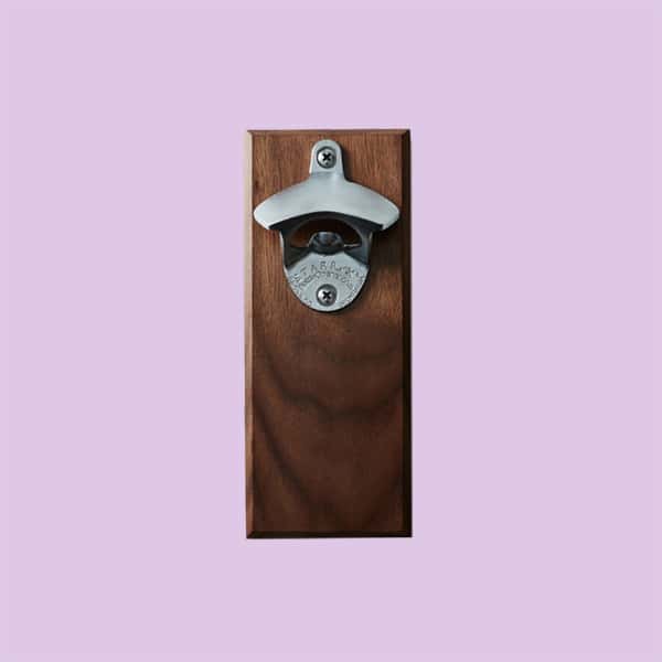A magnetic bottle opener on a piece of wood, on a light purple background.