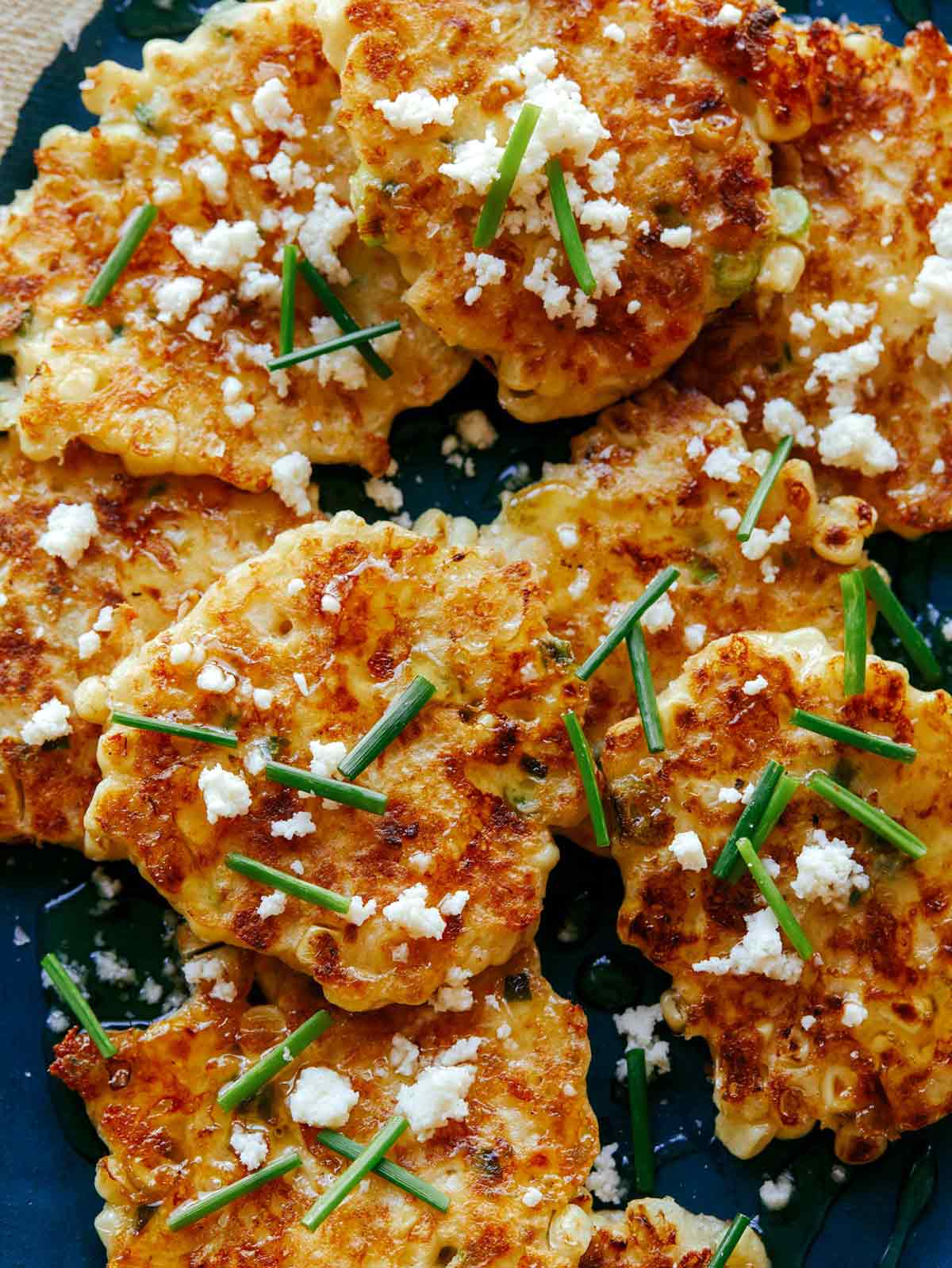 Close up shot of cheesy, buttery, Jalapeño corn cakes topped with honey, chives, and Cotija. 