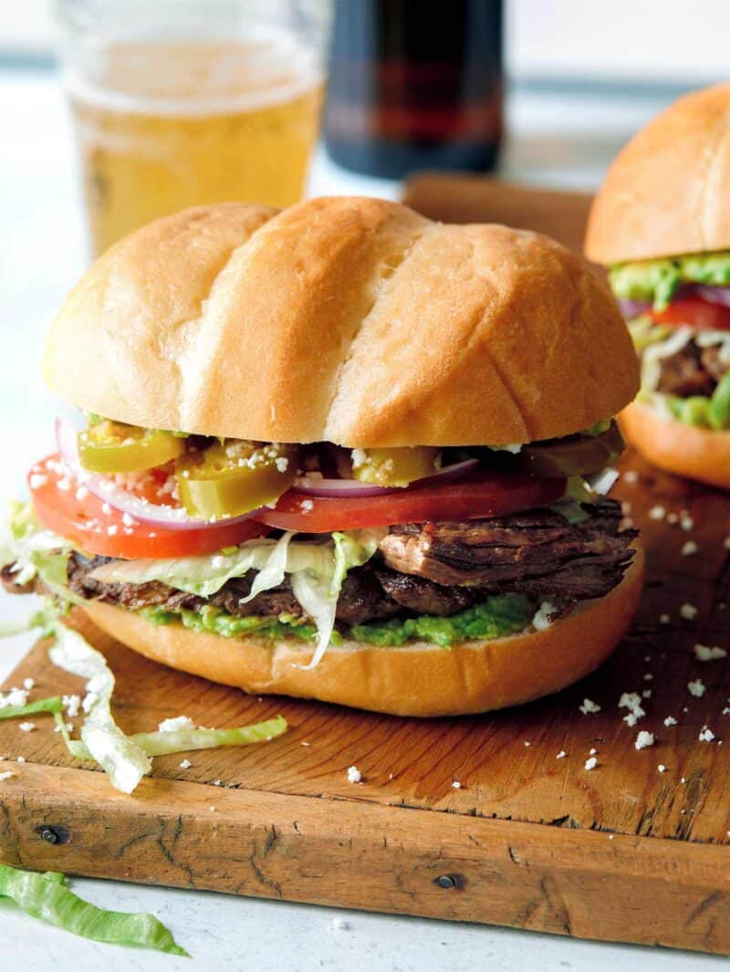 A Carna Asada Torta on a cutting board with a beer in the background.