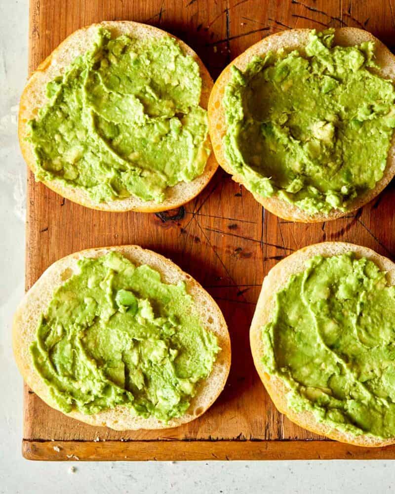 Smashed avocado overhead on a roll preparing a carne asada sandwich