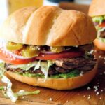 Carne Asada Torta on a cutting board with a beer in the background.