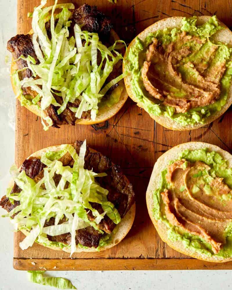 The making of a carne asada sandwich over head with shredded lettuce