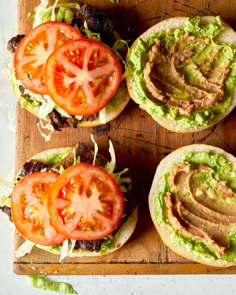 Adding tomatoes to a open faced carne asada sandwich in the making