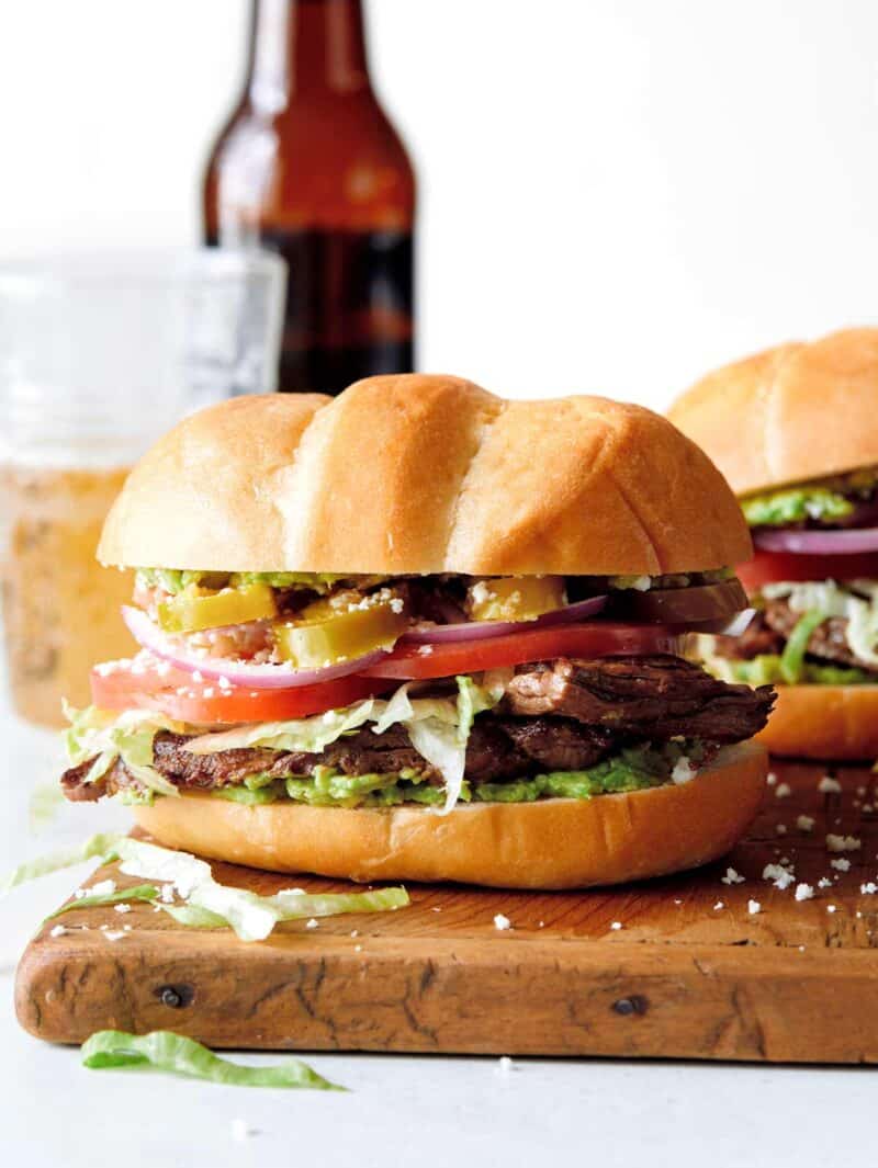 Carne Asada torta on a cutting board with a beer in the background. 