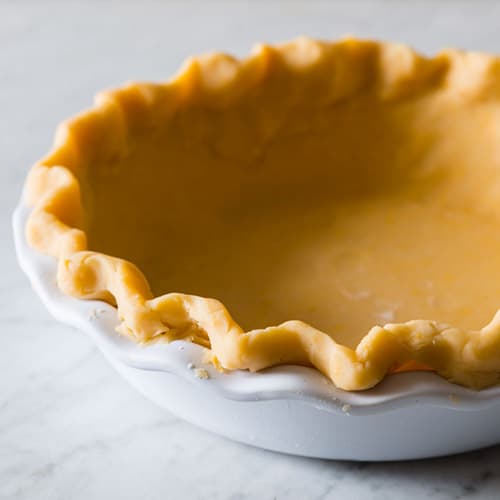 A close up of raw cheddar crust in a white pie dish.