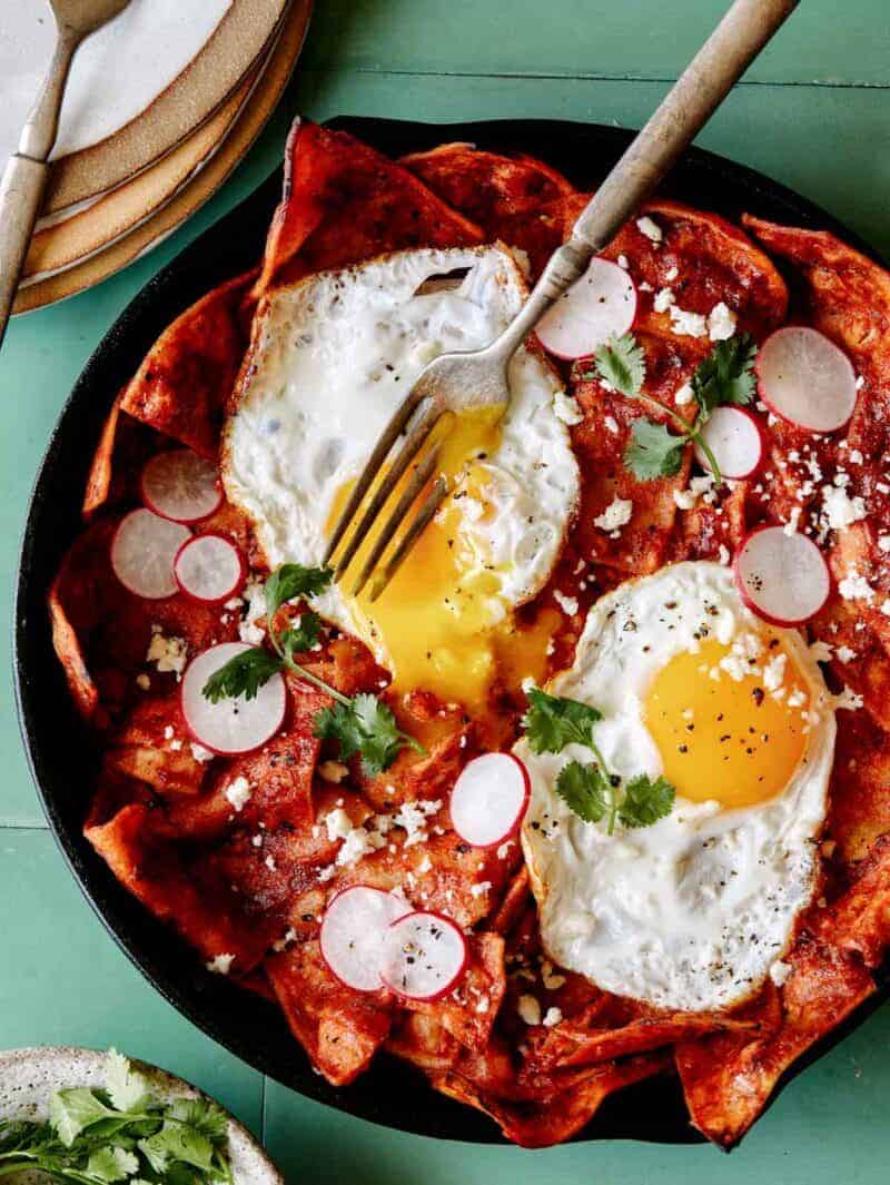 Chilaquiles with two fried eggs on top in a cast iron skillet with a fork. 