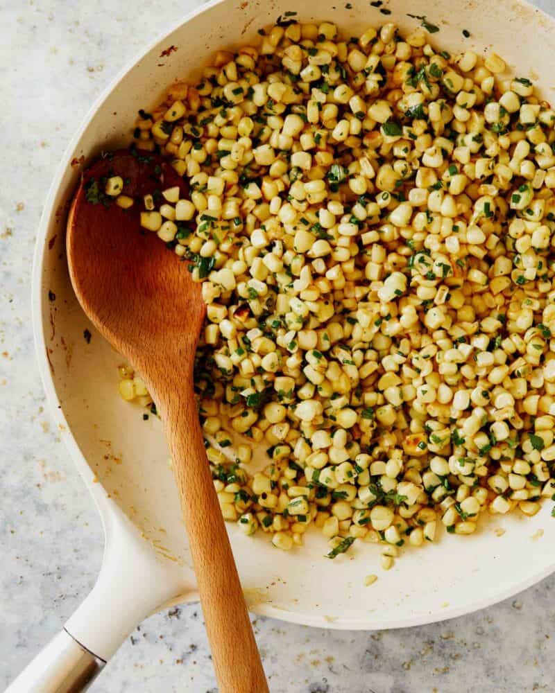 Summer corn salad with halloumi in a skillet being mixed together. 
