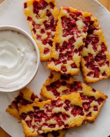 Mini strawberry cornmeal cobblers next to a bowl of whipped cream.