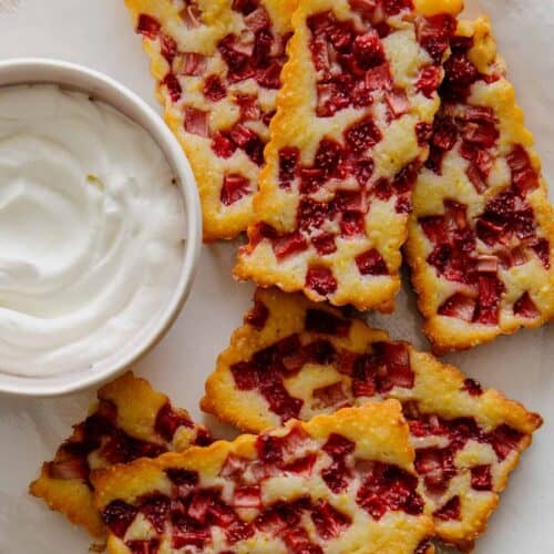 Mini strawberry cornmeal cobblers next to a bowl of whipped cream.