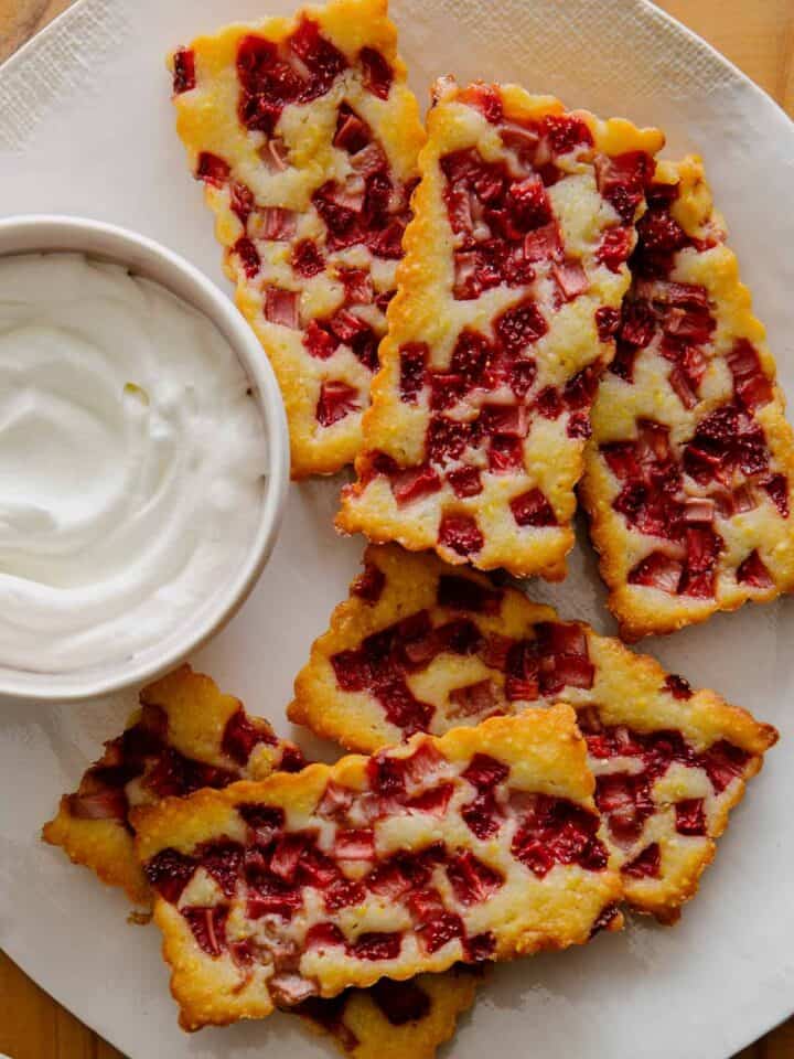 Mini strawberry cornmeal cobblers next to a bowl of whipped cream.