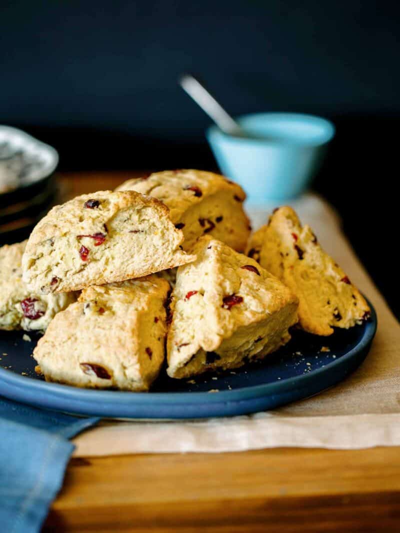 A close up of a plate of cranberry orange scones with blue bowl and spoon.