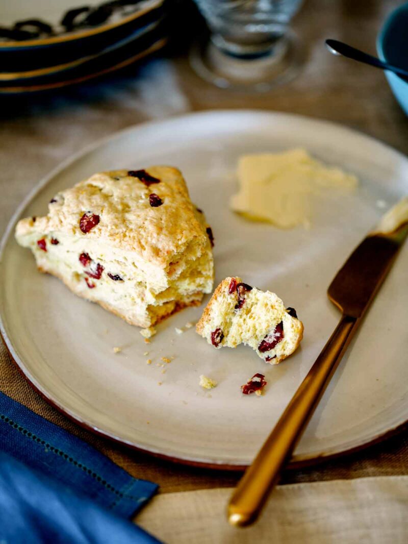 A close up on one Cranberry Orange scone broken open with butter smeared on them.