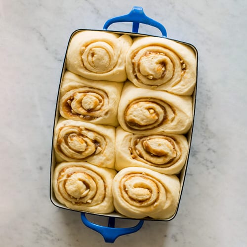 Blue rectangular pan of raw cinnamon rolls.