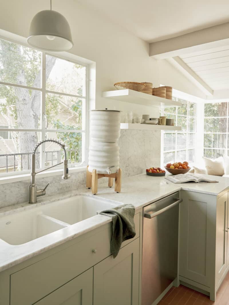 A kitchen sink by a window, Bosch dishwasher below with water filter on the counter. 
