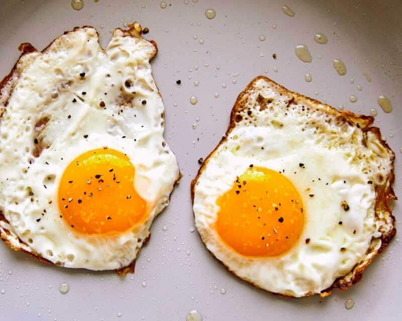 A close up of fried eggs in a non stick skillet with salt and pepper.