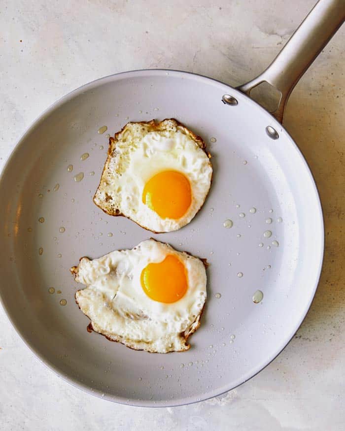 Freshly fried eggs in a non stick skillet showing the crispy edges of the eggs.