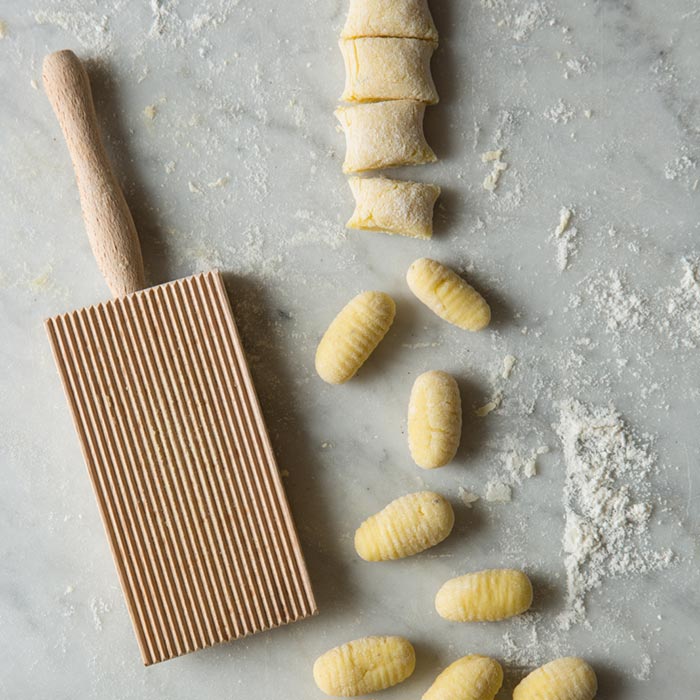 Raw gnocchi cut next to a gnocchi paddle.