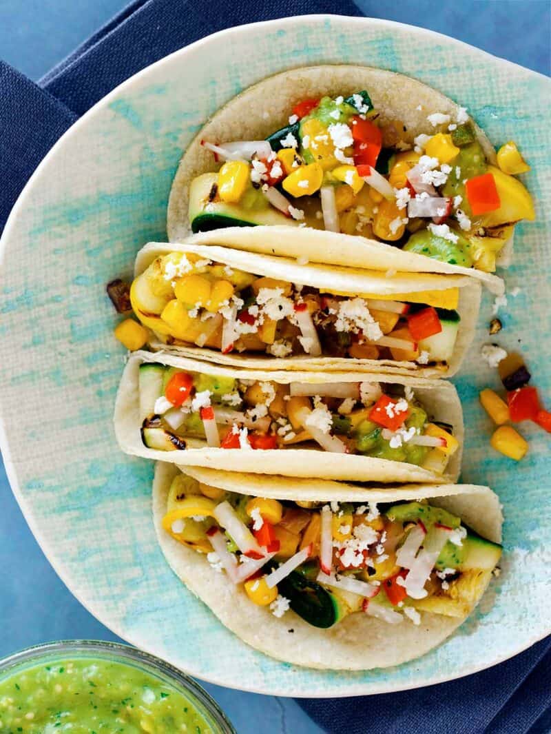 Four Grilled Zucchini tacos with toppings and tomatillo salsa on a plate. 