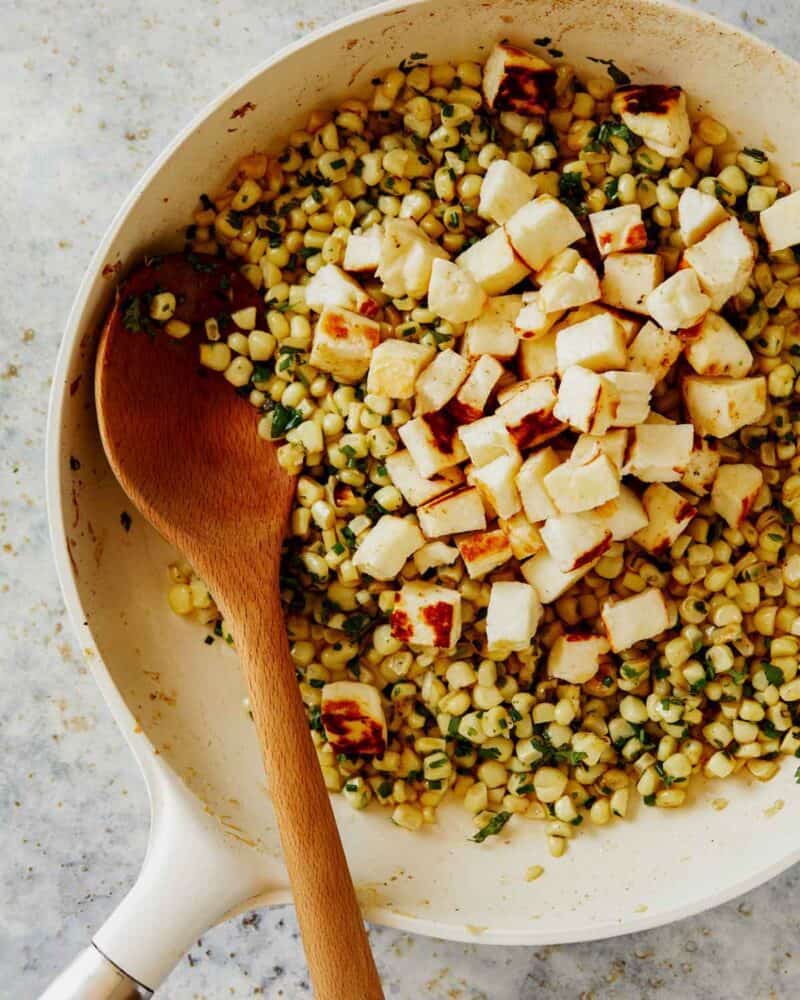 Fresh herbs and corn with curbed halloumi in a skillet.