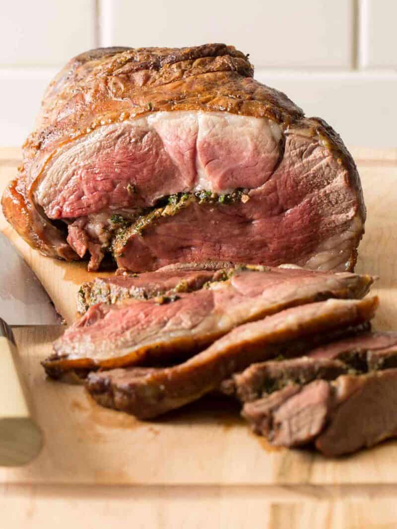 A close up of sliced, grilled lambchetta on a cutting board with a knife.