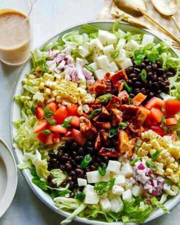 Loaded BBQ chicken salad on a plate with dressing on the side.