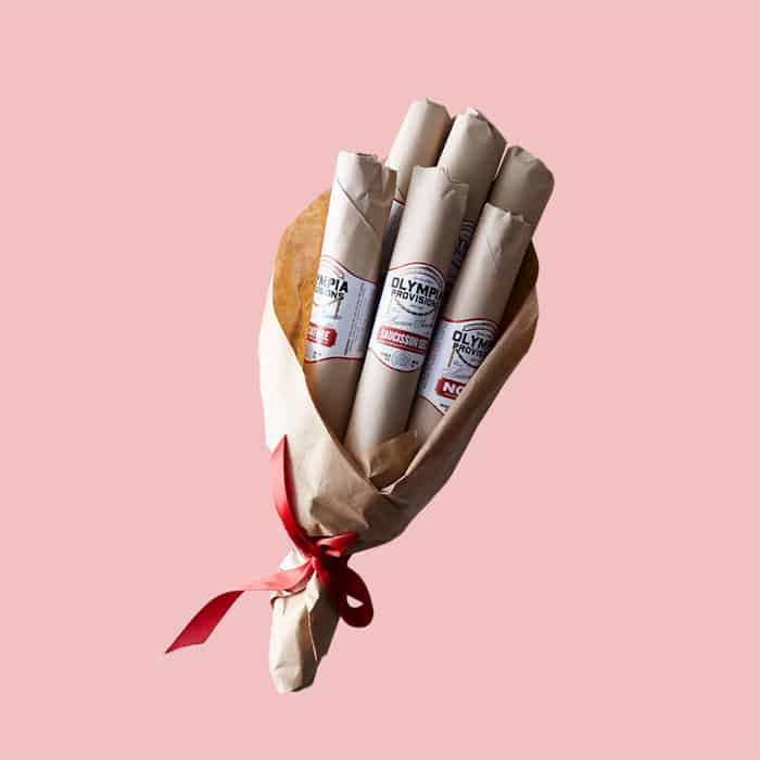 A bouquet of 6 salamis to be given as a gift on a solid pink background.