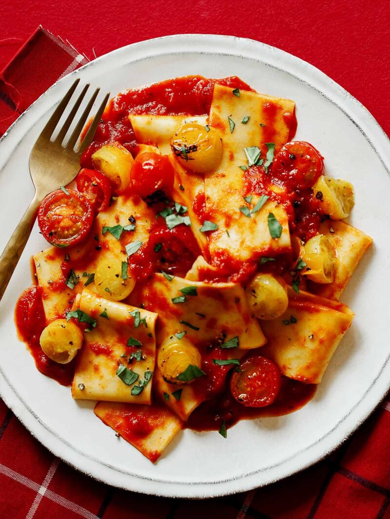 A plate of pappardelle pasta with cherry tomato sauce and a fork.