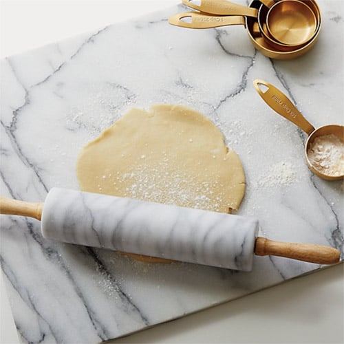 Marble cutting board and rolling pin, rolling out dough with measuring cups nearby. 