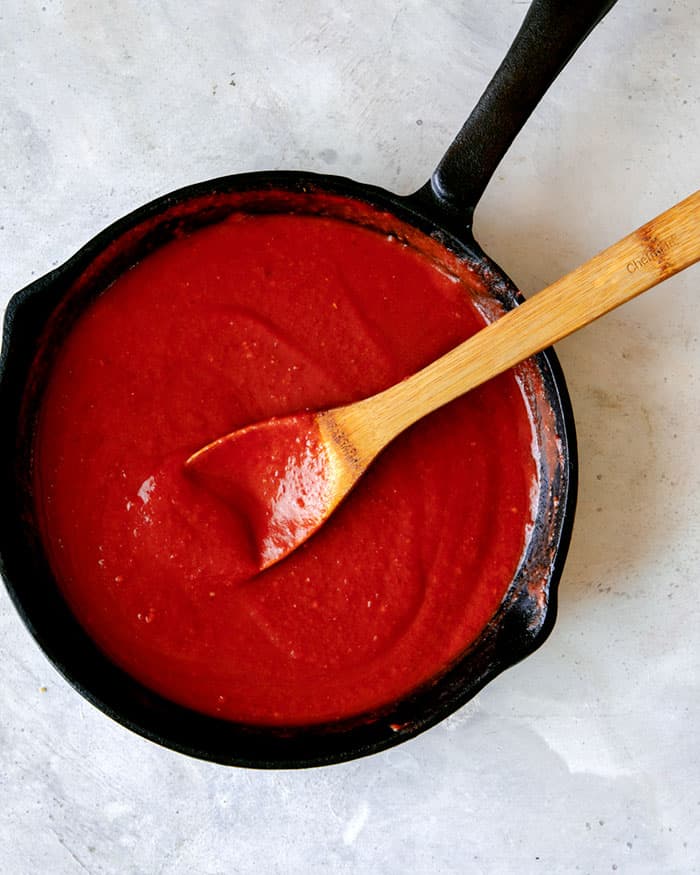 Blended ingredients to make a red sauce simmering in  a skillet. 