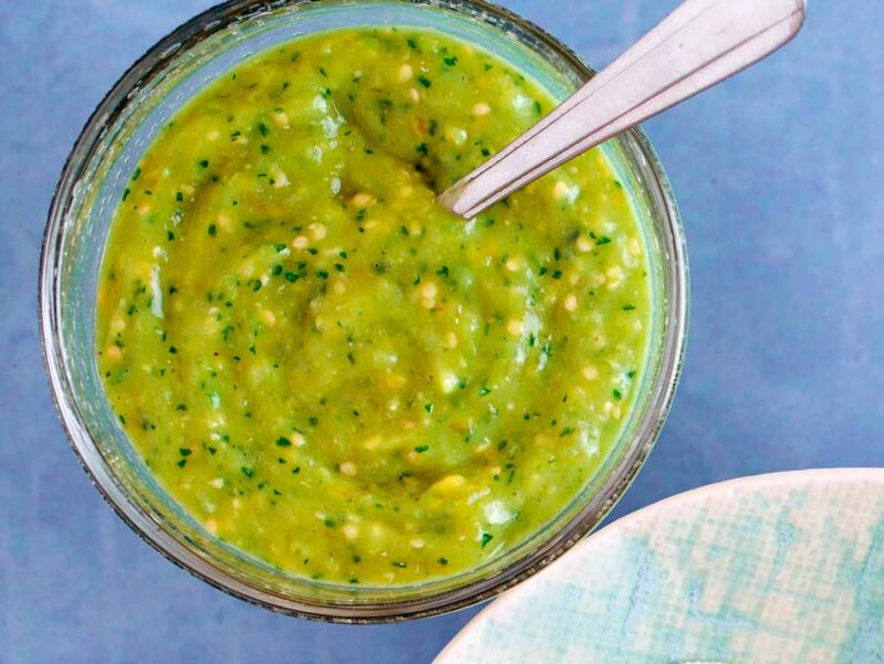 A jar of freshly made tomatillo salsa with a spoon in it.