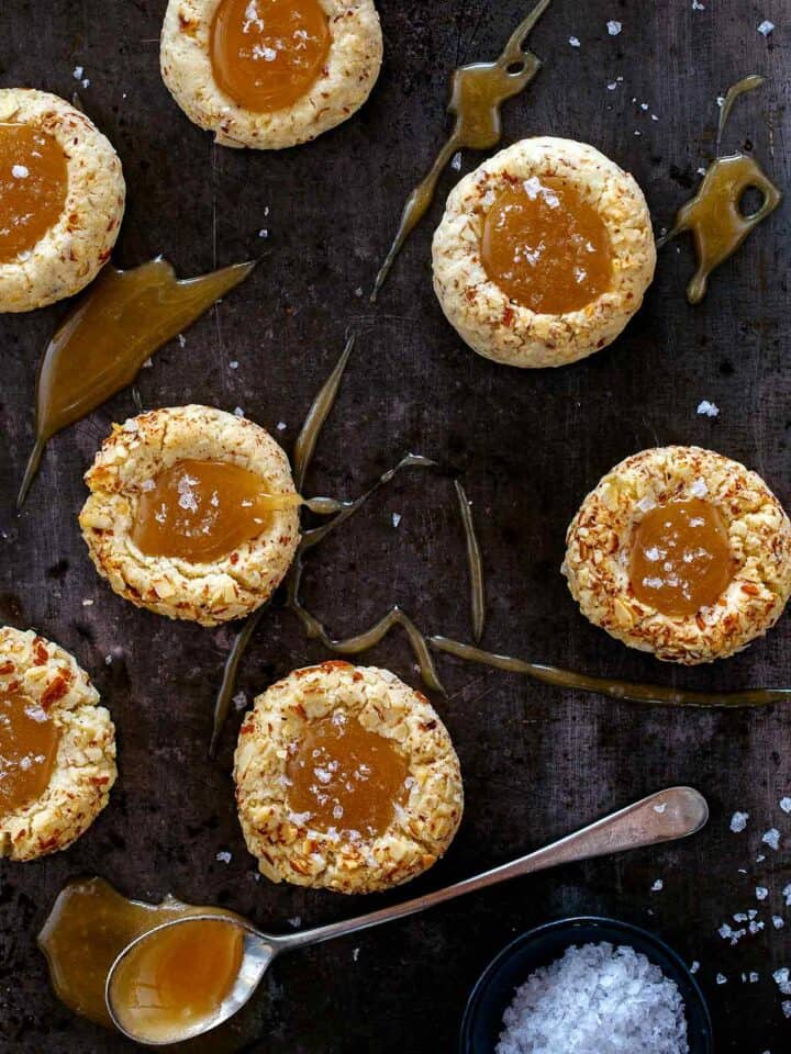 A close up of salted caramel thumbprint cookies on a dark surface with a spoon.