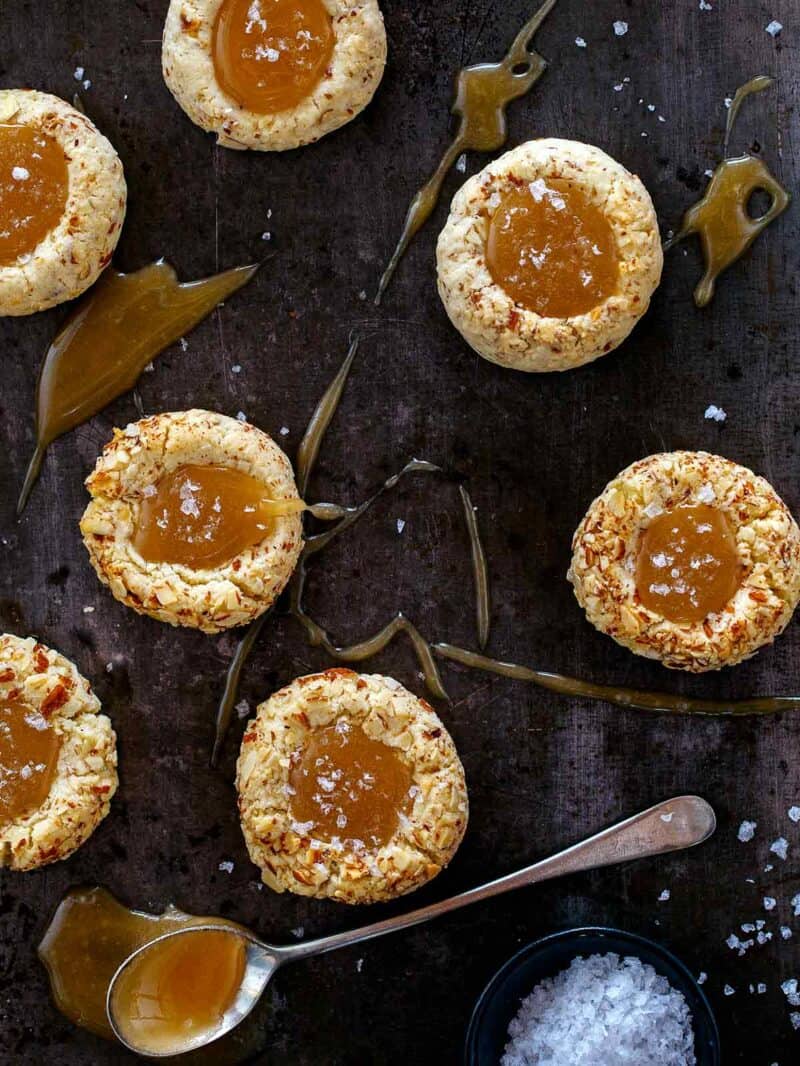 A close up of salted caramel thumbprint cookies on a dark surface with a spoon. 