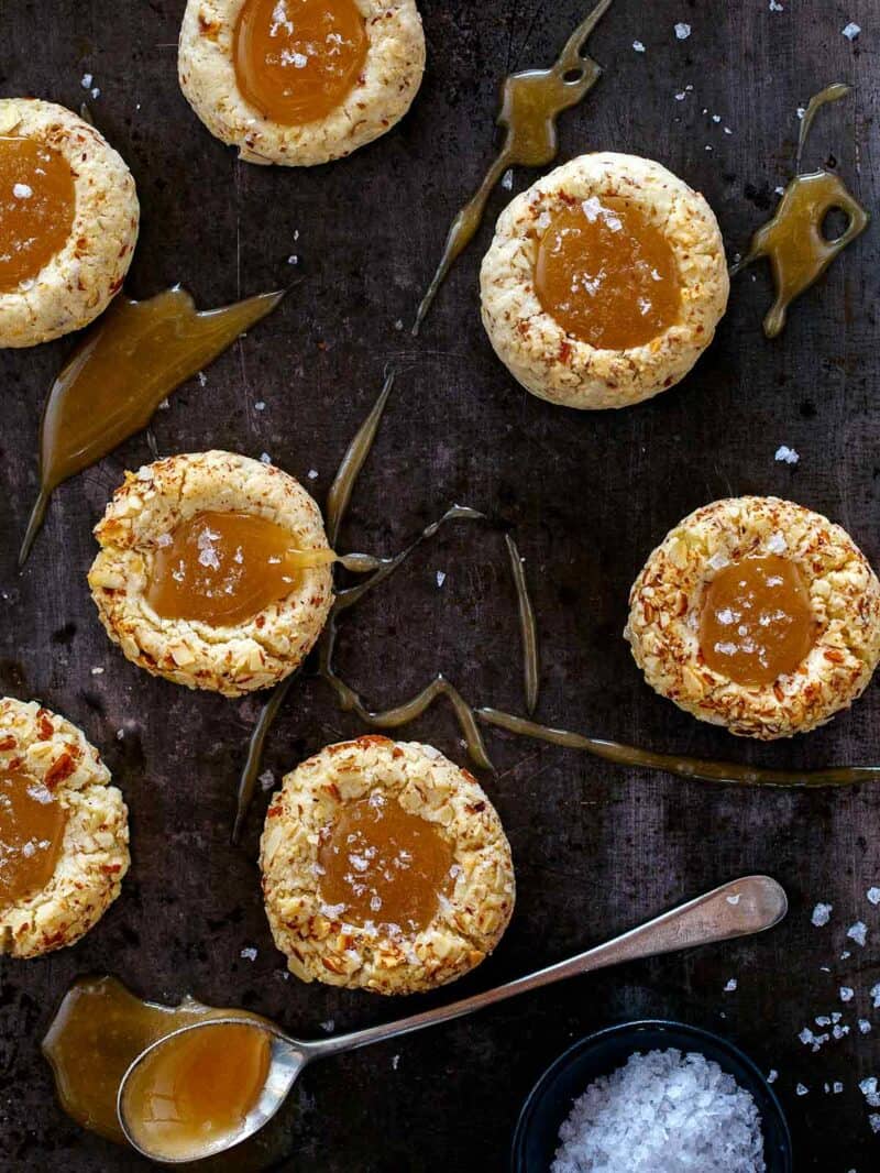 Salted Caramel Almond Thumbprint cookies getting sprinkled with salt. 