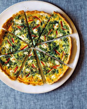 A whole sliced spinach quiche on a plate.