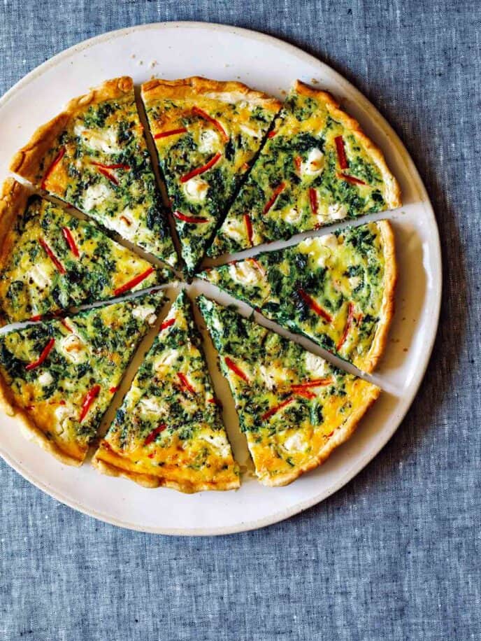 A whole sliced spinach quiche on a plate.