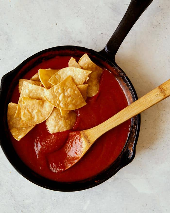 Fresh tortilla chips being added into a skillet with sauce for chilaquiles.